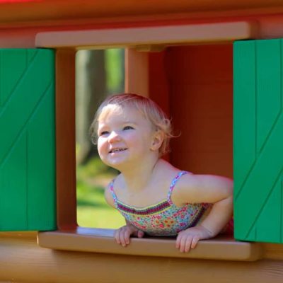petite fille à la fenêtre de sa cabane de jardin en plastique pour enfant