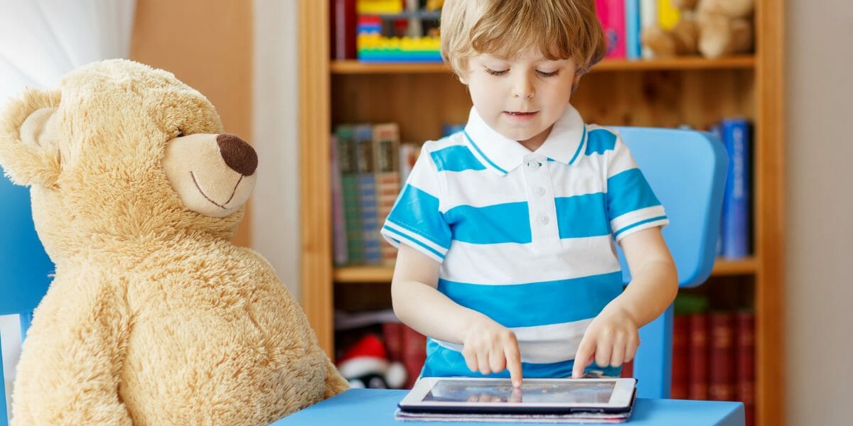 enfant qui joue avec sa tablette numérique et son ours en peluche