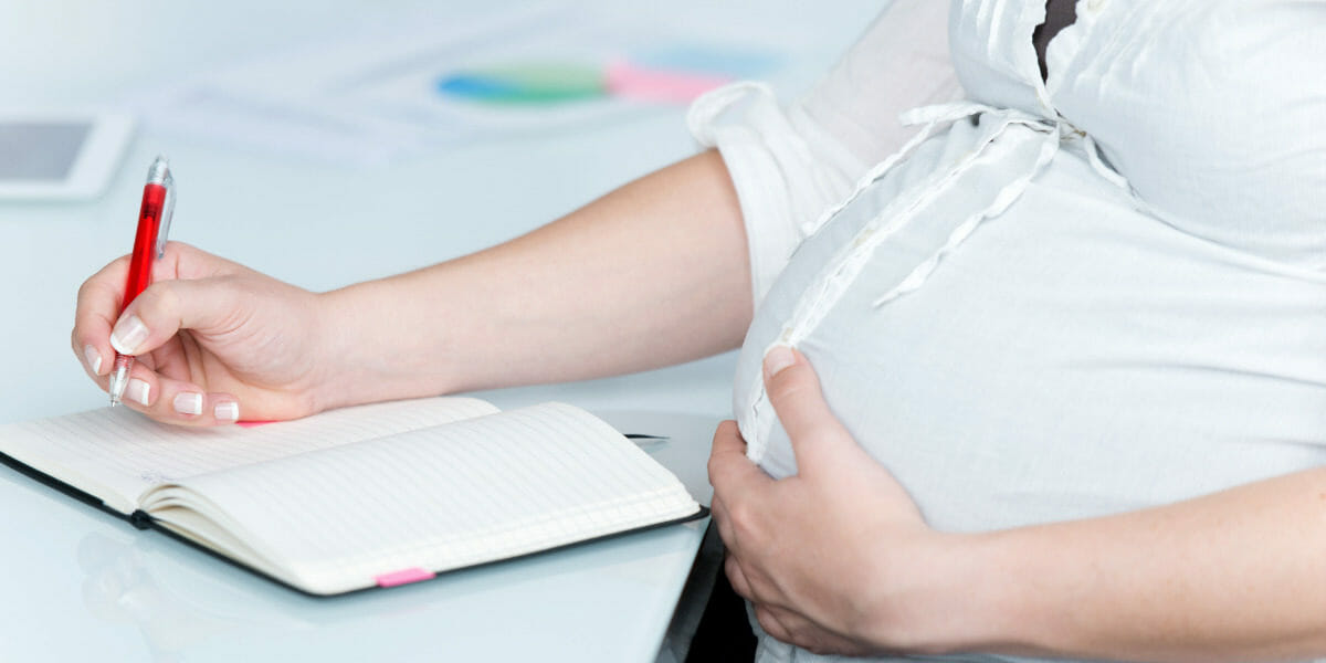 femme-enceinte-ecrivant-dans-un-livre-au-bureau